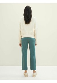 Overmaat crèmekleurige geribde trui, gecombineerd met teal brede broek en beige plateau schoenen, van achteren getoond tegen een neutrale achtergrond.