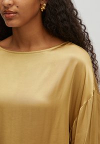 Goldener Satin-Oberteil mit einem lockeren, fließenden Design, weitem Ausschnitt und weicher Textur. Verfügt über eine glatte Oberfläche und weite Ärmel.