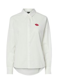 Camisa de algodón blanca de botones con mangas largas, que presenta un bordado de labios rojos en el lado izquierdo del pecho y un dobladillo curvado.