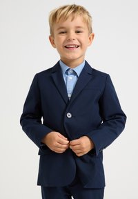 Mørkeblå blazer med et slankt design, enkelt knappelukking og en lyseblå skjorte under. Glatt stofftekstur.