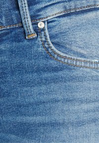 Jean en denim bleu délavé avec une poche visible, des coutures contrastantes couleur miel et un détail de rivet métallique près de la ceinture.