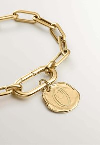 Collar de cadena de oro con eslabones sobredimensionados y un colgante circular texturizado que presenta un diseño de espiral grabado. Superficie lisa y brillante.
