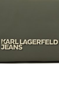 Tmavě zelená taška s raženým textem "KARL LAGERFELD JEANS" v bledých písmenech, hladký povrch, obdélníkový tvar.