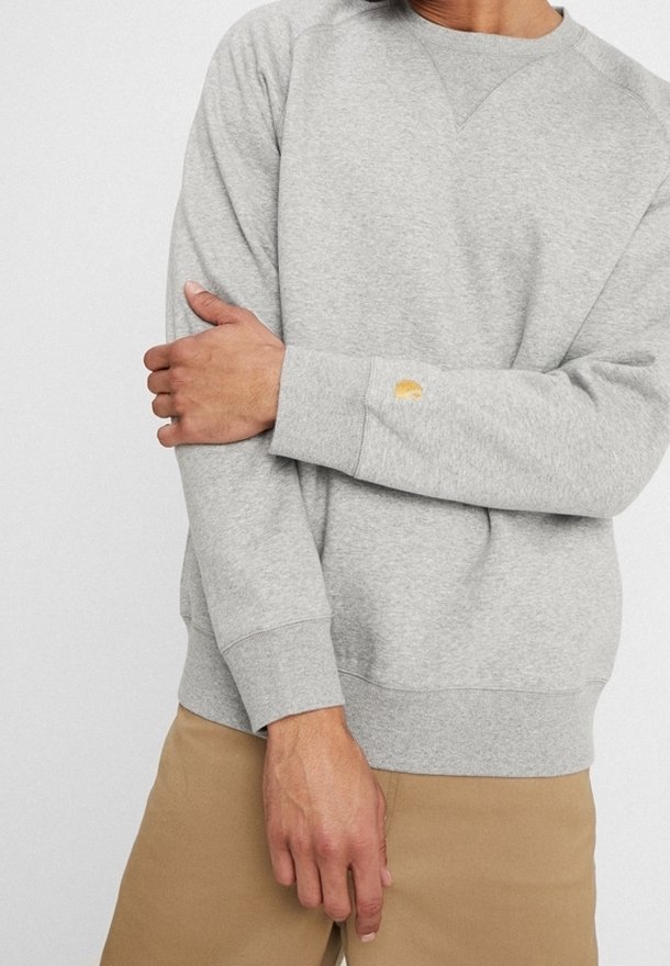 Szary bawełnowy sweatshirt z okrągłym dekoltem, ściągaczami przy rękawach i u dołu. Zawiera małe logo na nadgarstku. Model nosi khaki spodnie.