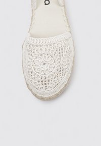 Espadrille blanca con un intrincado diseño de encaje, puntera redondeada y suela de yute trenzado. Presenta un patrón texturizado y detalles de costura resistentes.