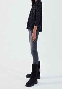 Maglietta nera a maniche lunghe con texture, abbinata a jeans skinny grigi e stivali neri in suede al ginocchio con suola spessa.
