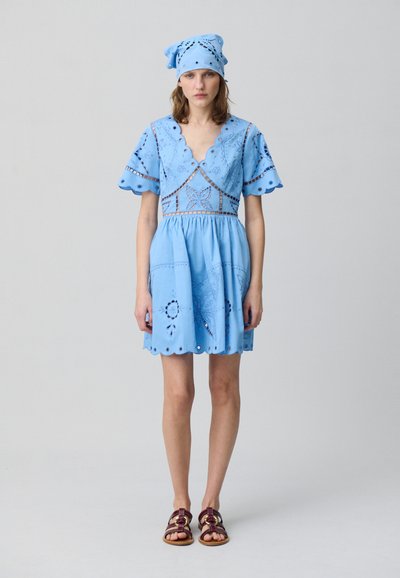 Vestido de algodón azul claro con mangas y dobladillo en forma de onda, bordado floral y cintura ajustada. Combinado con un pañuelo a juego.