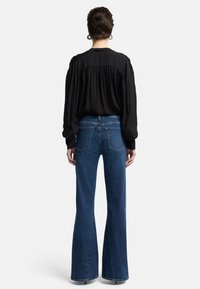 Zwarte, vloeiende blouse met geplooide achterkant, gecombineerd met wijd uitlopende, medium blauwe jeans. Glad oppervlak, omgeslagen mouwen, klassiek denimontwerp.