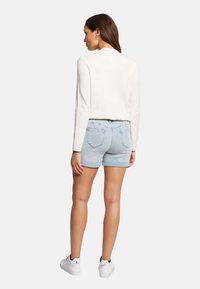 Un haut à manches longues blanc associé à un short en denim bleu clair et des baskets blanches. La tenue est simple, sans motifs ni accents notables.