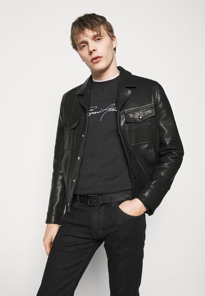 Czarna skórzana kurtka z dwoma przednimi kieszeniami, noszona na ciemnoszarym swetrze. Czarne dżinsy i pasek dopełniają stylizację. Proste tło.