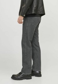 Jeans de denim gris con corte recto, costuras visibles y bolsillos traseros, combinados con botas negras con cordones y una chaqueta de cuero.