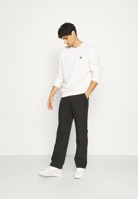 Felpa rosa chiaro con un piccolo logo giallo, pantaloni neri e sneakers bianche. La felpa presenta polsini a coste e un collo rotondo.