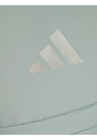 Tejido deportivo verde claro con una textura suave que presenta un logotipo de tres franjas en plata metálica, colocado sobre una superficie plana.