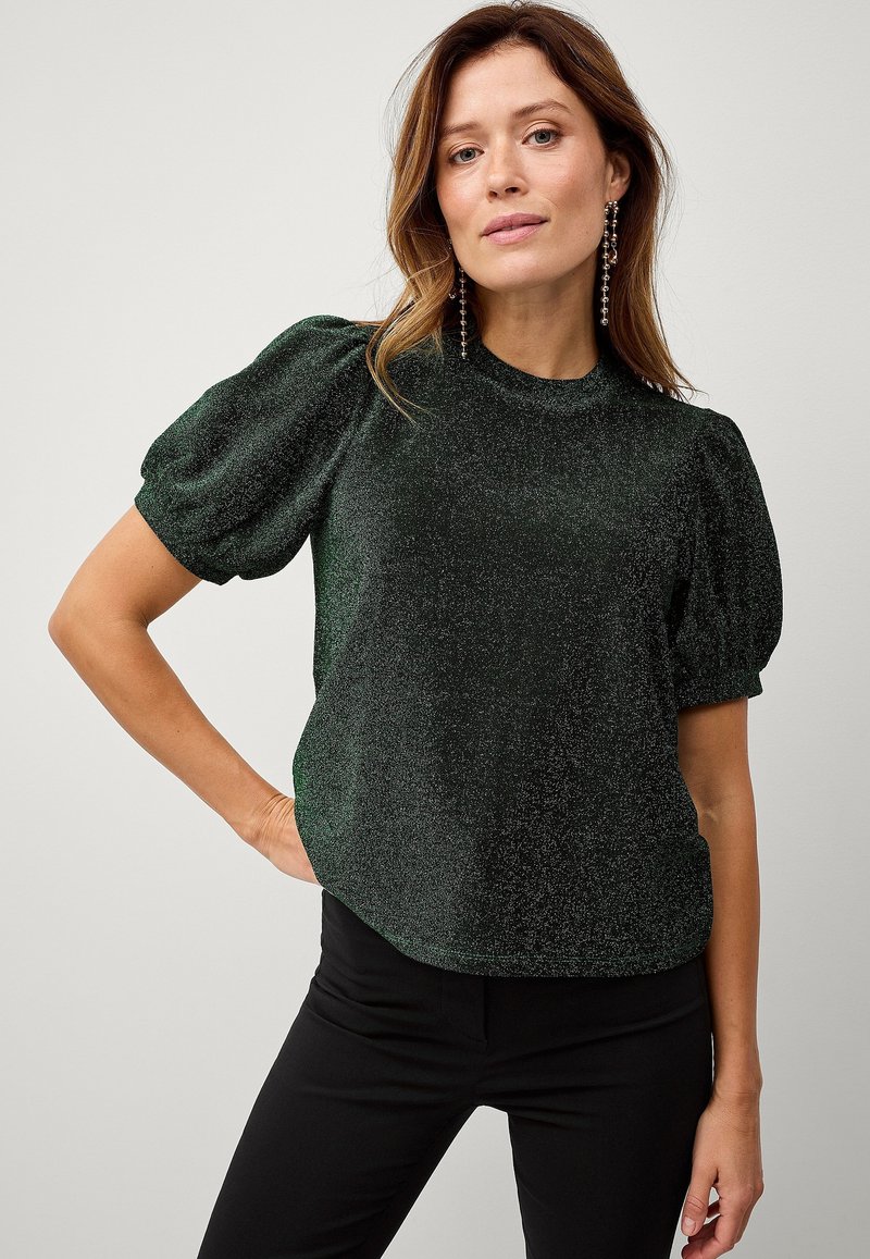 Groen sprankelend topje met korte puffmouwen, een hoge halslijn en een ontspannen pasvorm. G gedragen met zwarte broeken, met een gladde textuur.