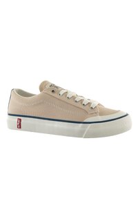 Zapatillas de lona beige con suela de goma blanca, franja de acento azul marino, cordones tradicionales y punta texturizada. Parche de logo rojo en el talón.