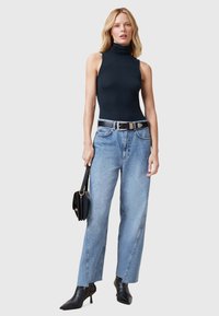 Bodysuit negro de cuello alto, vaqueros de pierna recta azul claro, cinturón negro y botas negras de tacón puntiagudas. Lleva un bolso negro.