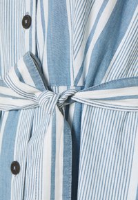 Blå och vit randig skjorta med korta ärmar, med knappstängningar och ett knytbälte i midjan, tillverkad av ett lätt material.