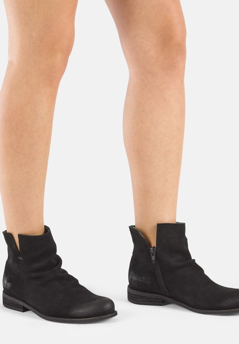 Botines de ante en negro con un diseño holgado. Cuentan con un cierre lateral y un tacón bajo apilado. Textura suave con un ligero brillo.