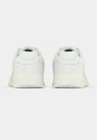 Baskets en cuir blanc avec un bout rond, un design minimaliste, un col rembourré et une semelle en caoutchouc texturé blanc. Vue de l'arrière.