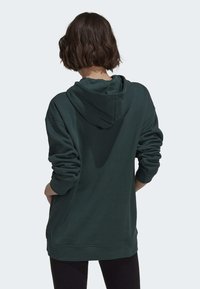 Mörkgrön hoodie med lös passform, långa ärmar och textilstruktur. Har en känguruficka och ribbad mudd.