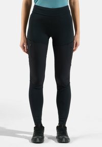 Leggings noirs extensibles avec une taille haute, des poches latérales et une coupe ajustée. Le tissu semble lisse avec une texture subtile.