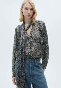 Geometrisesti kuvioitu paita mustassa, harmaassa ja valkoisessa, löysällä istuvuudella, V-pääntiellä ja pitkällä solmukkeella. Yhdistetty korkeavyötäröisten denim-farkkujen kanssa.