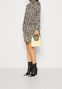 Animal print dress in beige, black, and cream; long sleeves; cinched waist. Yellow handbag with curved handle. Black heeled boots with silver toes.