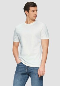 Weißes T-Shirt mit kurzen Ärmeln und Rundhalsausschnitt. Aus glattem Stoff gefertigt. Getragen mit blauen Jeans. Einfaches Design ohne auffällige Logos.