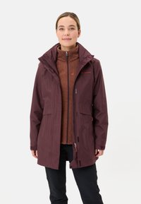 Bordeaux waterdichte jas met rits aan de voorkant, capuchon en twee zijzakken, gecombineerd met een bruine fleece binnenlaag, gedragen door een model.