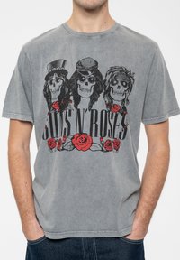 Gray cotton t-shirt featuring a front graphic of three skulls wearing hats, with "GUNS N' ROSES" text and red roses accents.