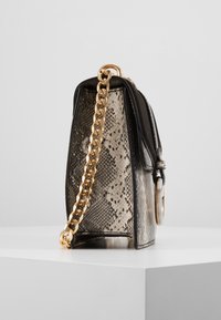 Malá kabelka s hadím vzorem v šedé a černé barvě, s zlatým řetízkovým popruhem a hladkým koženým detailem na vrchu.