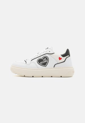 Sneaker in pelle bianca con dettagli neri, caratterizzati da un grande logo a forma di cuore e il testo "LOVE MOSCHINO". Suola in gomma spessa con dettaglio a forma di cuore rosso.