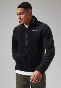 Black fleece jacket with a zipper and a high collar. Features two side pockets and an embroidered logo on the chest. Soft texture.