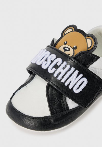 Svart och vit sneaker i lädermaterial, med ett björngesicht på remmen och broderad "Moschino"-logotyp. Rundad tådesign.
