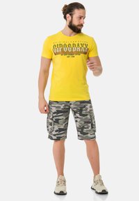 Geel katoenen t-shirt met bedrukte tekst en grafisch ontwerp, gecombineerd met grijze camouflage cargo shorts met zijzakken en een relaxte pasvorm.