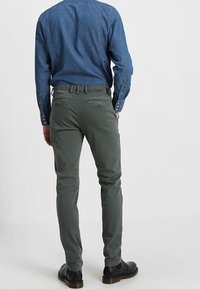 Zelené kalhoty z bavlněného kepru s úzkým střihem, bočními kapsami a zadními náprsními kapsami. V kombinaci s modrou džínovou košilí a černými botami.