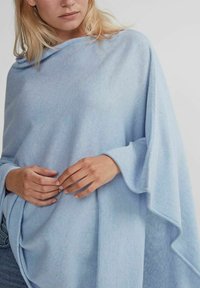 Ljusblå stickad poncho med en draperad design, mjuk textur och vida ärmar, med ett subtilt och jämnt stickat mönster.