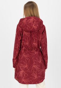 Giacca rossa impermeabile con un motivo di piante rosa chiaro, cintura regolabile in vita e cappuccio. Caratterizzata da maniche lunghe e lunghezza fino a metà coscia.