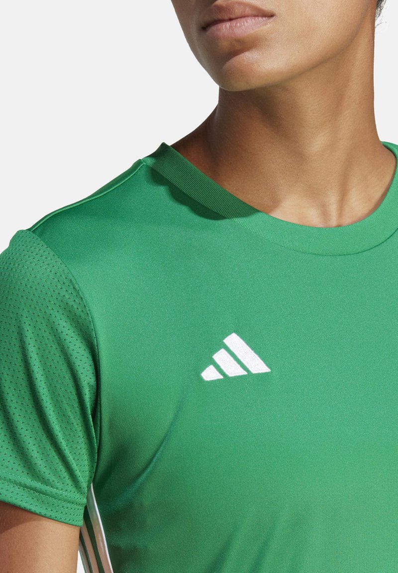 T-shirt de sport vert avec un col rond, en tissu respirant. Présente le logo Adidas blanc sur l'épaule droite. Vue en gros plan.
