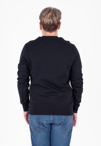 Czarna bluza z długim rękawem, okrągłym dekoltem i ściągaczami; noszona z niebieskimi dżinsami, prezentująca prosty, gładki design.