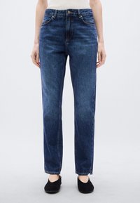 Μπλε τζιν παντελόνι με ίσια γραμμή, πέντε τσέπες, κλείσιμο με κουμπιά και ελαφρώς ξεθωριασμένο πλύσιμο. Το ύφασμα φαίνεται μαλακό με λεία υφή.