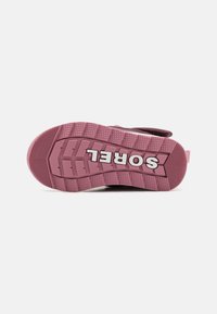 Semelle en caoutchouc rose clair avec des motifs de traction texturés, arborant un logo "SOREL" blanc et une forme contournée pour plus de stabilité.