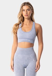 Gaiši zils sporta krūšturis ar ribotu jostu un logo detaļu, apvienots ar saskaņojošām augstām legingām līdzīgā audumā un krāsā.