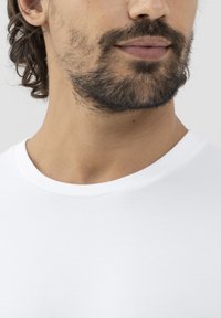 Bílý bavlněný tričko s kulatým výstřihem. Tkanina působí hladce s mírným leskem a zachycuje kontury krku a brady.