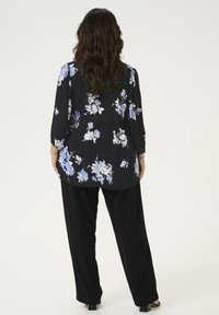 Zwarte bloes met blauwe en witte bloemen, driekwartmouwen en een vloeiende pasvorm, gecombineerd met losse zwarte broeken en zwarte schoenen.