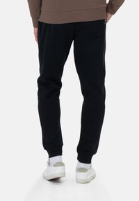 Zwarte sweatpants met een ontspannen pasvorm, voorzien van elastische boorden en een detail op de achterzak, gecombineerd met witte sneakers en een zichtbare geribbelde tailleband.