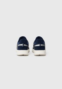 Tenis azul marinho com parte superior em tecido texturizado, tiras de accentuação prateadas e sola branca em borracha; projetados para conforto e uso casual.