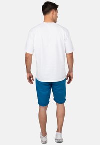 Witte korte mouwen t-shirt, gecombineerd met opgerolde turquoise shorts en witte sneakers. Eenvoudig ontwerp, katoenmateriaal en een ontspannen pasvorm.