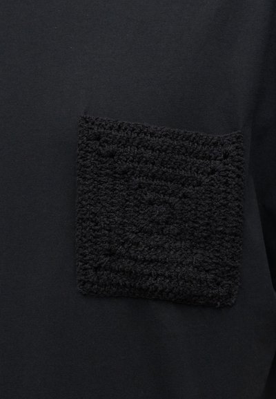 Μαύρο ύφασμα με υφή, αφράτη τετράγωνη τσέπη ραμμένη πάνω σε λείο φόντο υφάσματος.
