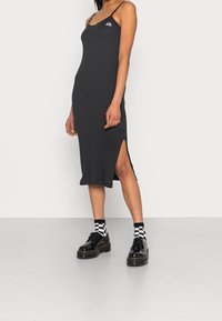 Czarna, prążkowana sukienka midi na cienkich ramiączkach, z bocznymi rozporkami i małym logo na klatce piersiowej. Zestawiona z błyszczącymi czarnymi butami na platformie i w kratkę skarpetkami.